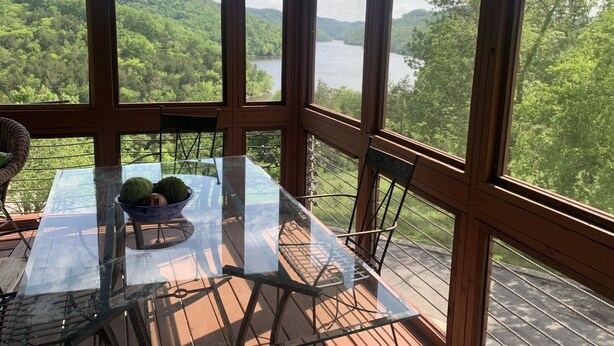 Une terrasse en bois avec une table et des chaises en verre, donnant sur une forêt et un lac.
