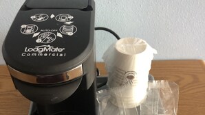 Una cafetera, una cápsula de café y una bandeja sobre una mesa.