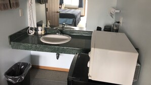 Un baño de hotel con lavamanos, espejo, secador de pelo y un cubo de basura.