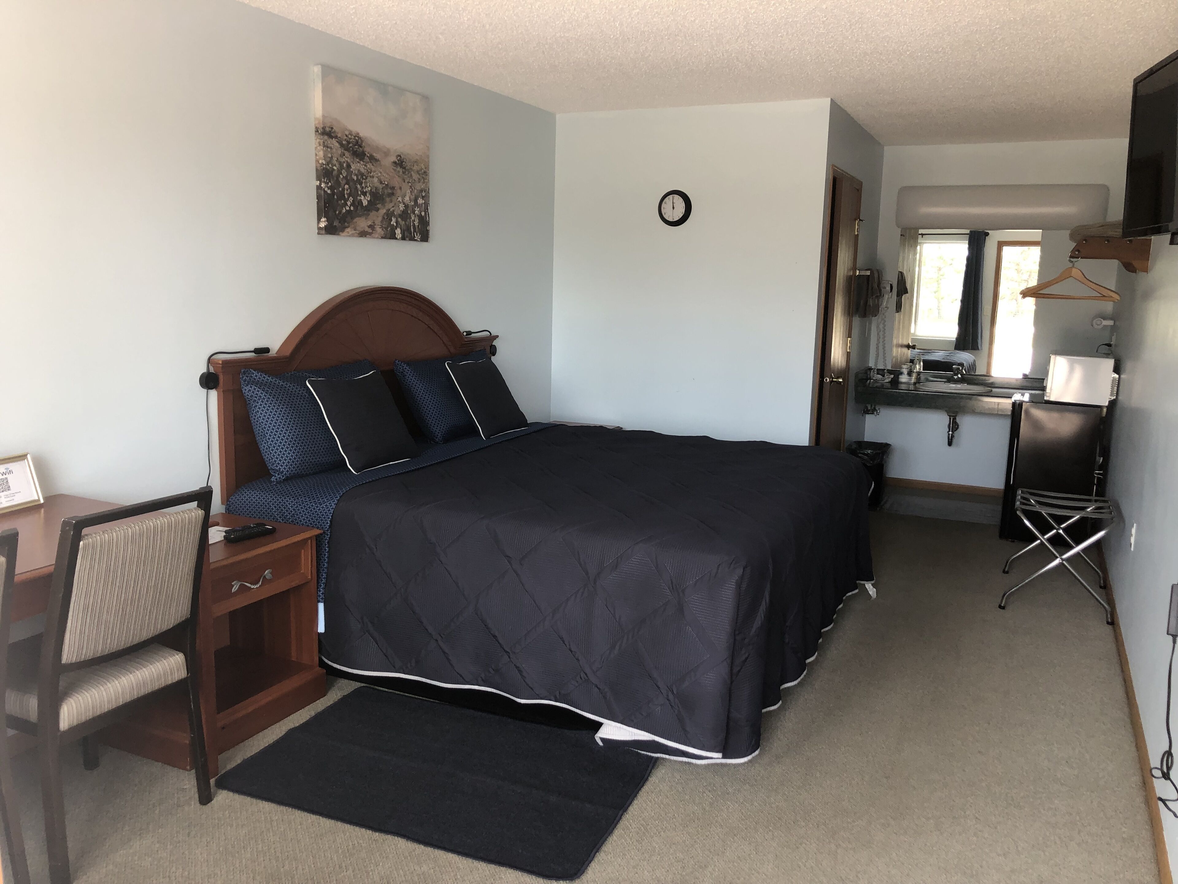 A bedroom with a bed, bedside table, chair, and a small desk with a chair.