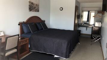 A bedroom with a bed, bedside table, chair, and a small desk with a chair.