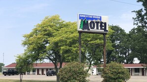 Letrero de motel con un gráfico de montaña, rodeado de árboles y un edificio al fondo.