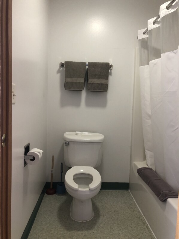 Un baño pequeño con inodoro, un perchero con dos toallas, un dispensador de papel higiénico y una cortina de ducha.
