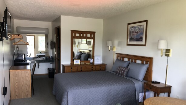 Habitación de hotel con una cama grande, un escritorio, una silla, una mesita, un espejo y un cuadro en la pared.