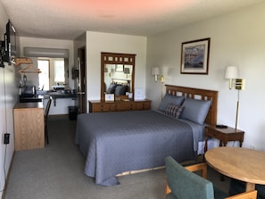 Habitación de hotel con una cama grande, un escritorio, una silla, una mesita, un espejo y un cuadro en la pared.