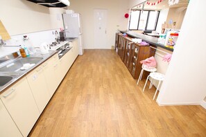 A kitchen with wooden flooring, a refrigerator, a sink, and a countertop with various items.