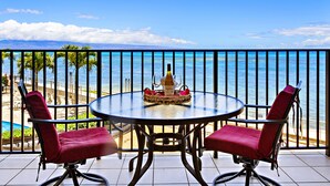 Un balcon avec une table ronde et deux chaises, donnant sur une plage et l’océan.