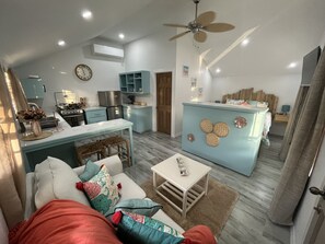A modern kitchen with a dining area, a living room with a sofa and coffee table, and a bedroom with a bed and nightstand.