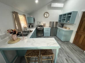 A compact kitchen with a central island, a sink, a stove, and a refrigerator. There are two wicker stools at the island.