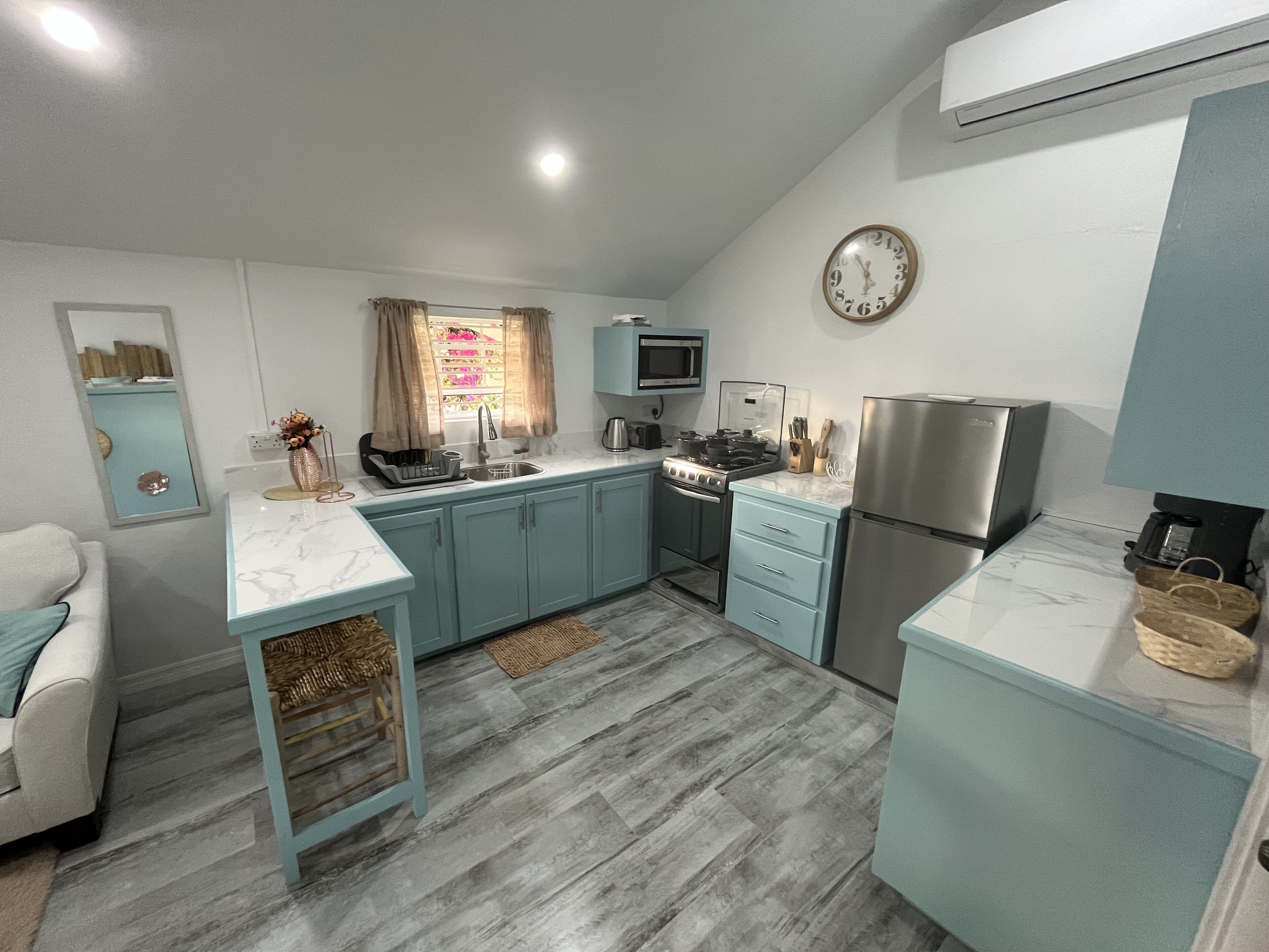A compact kitchen with teal cabinets, a stainless steel refrigerator, a microwave, and a stove.