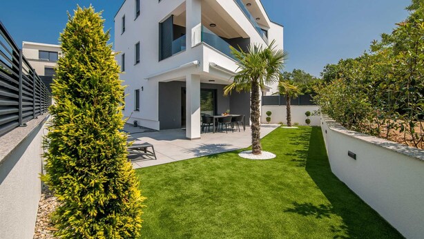 A modern two-story house with a flat roof, a patio with outdoor furniture, and a well-maintained lawn. - Apartment AK lux with private pool (Njivice)