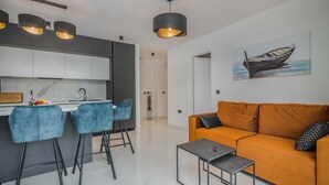 A modern kitchen with bar stools, a dining table, and pendant lighting. There is a sofa and a coffee table in the living area, and a painting on the wall. - Apartment AK lux with private pool (Njivice)
