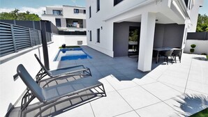A modern outdoor pool area with a sun lounger, a small table with chairs, and a clear blue pool. - Apartment AK lux with private pool (Njivice)