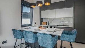 A modern kitchen with a central island, white cabinets, and blue bar stools. - Apartment AK lux with private pool (Njivice)
