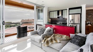Un salon moderne avec un canapé, un îlot de cuisine rouge et une vue sur la mer.
