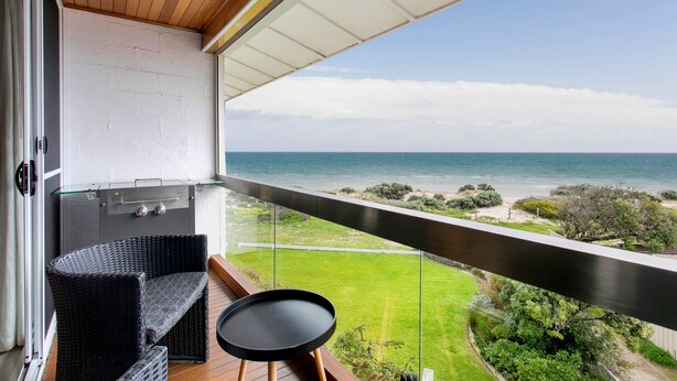 Un balcon avec vue sur l’océan, un barbecue, un canapé en osier et une petite table.