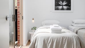 Une chambre moderne avec une porte vitrée donnant sur un balcon, une photographie encadrée accrochée au mur et des lits soigneusement faits.