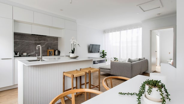 Une cuisine moderne avec des meubles blancs, un pare-feu en marbre et un îlot central doté de tabourets.
