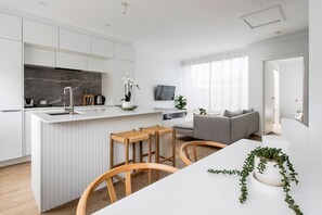 Une cuisine moderne avec des meubles blancs, un pare-feu en marbre et un îlot central doté de tabourets.