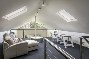 Relax in this cozy attic room with a comfortable sofa, coffee table, and desk, featuring a metal ladder to the loft area.