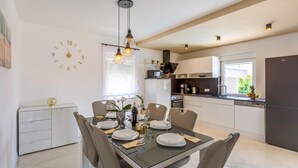 Une cuisine moderne avec des meubles blancs, un coin repas doté d’une table en verre et une horloge au mur.