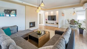 Un salon moderne avec un grand canapé d’angle, une table basse, une cheminée et un téléviseur fixé au mur.