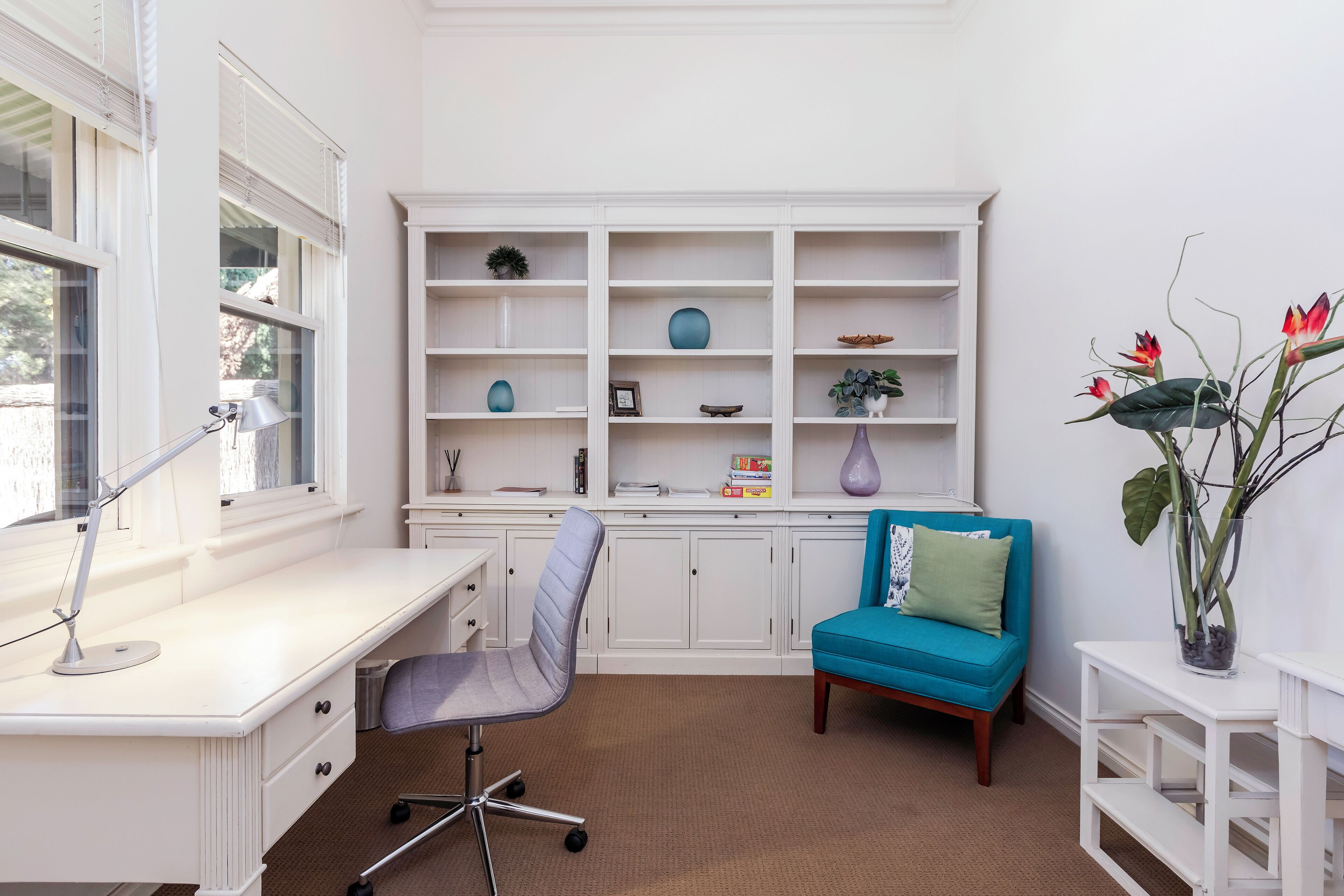 A room with a white desk, a blue chair, a teal sofa, and a white shelving unit with decorative items.