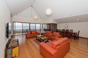 A spacious living room with orange sofas, a coffee table, and a large window overlooking the sea. - On The Beach - Glenelg, Sea Views, Cafes, Shopping (Glenelg North)