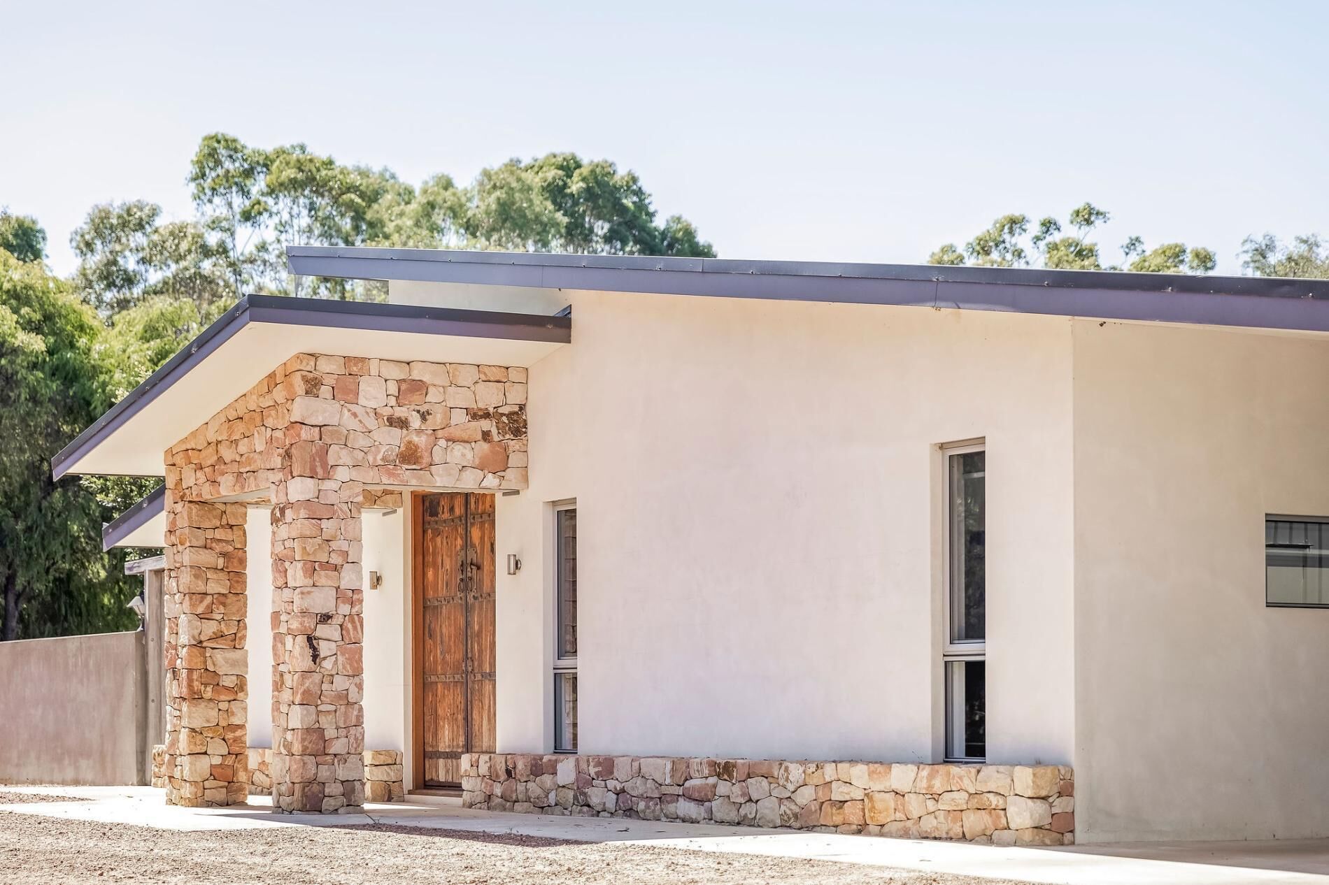 A modern house with a stone facade, a wooden door, and a covered porch.