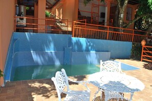 Una piscina con pared de azulejos azules, sillas blancas y barandilla naranja.