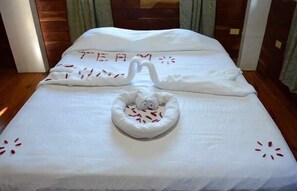 Un lit parfaitement fait, avec une serviette en forme de cygne et le mot « ÉQUIPE » brodé sur l’oreiller.