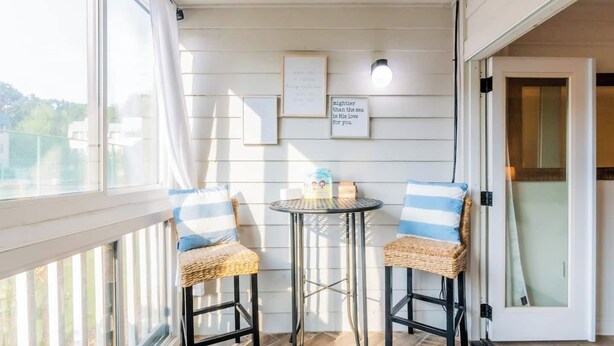 A balcony with two wicker chairs, a small round table, and a framed quote on the wall. - Coastal Villa by the Beach (Hilton Head Island)