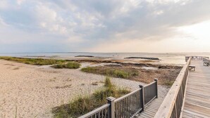 A beach with a wooden boardwalk leading to the water, featuring a sandy beach and grassy dunes. - Coastal Villa by the Beach (Hilton Head Island)