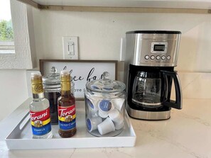 A kitchen counter with Torani syrup bottles, a jar of coffee pods, and a coffee maker.