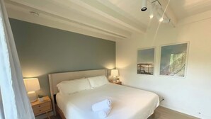 A neatly made bed in a room with a light blue wall, two bedside lamps, a small bedside table with a plant, and two framed pictures on the wall. - Encinitas Surf Shack w/ Private Rooftop Oasis (Encinitas)