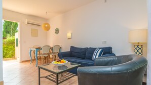Un salon avec un canapé bleu, une table basse en verre et un coin repas comprenant une table et des chaises.