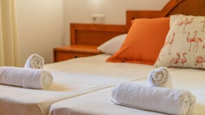 Une chambre d’hôtel avec deux lits, chacun recouvert d’une courtepointe blanche et agrémenté d’une serviette blanche roulée. Sur l’un des lits, on trouve un oreiller orange orné d’un motif de flamant rose.
