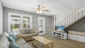 A living room with a sofa, a coffee table, a TV, and a staircase. - Emerald Coast Paradise Condo, Steps from PCB Beaches! (Panama City Beach)