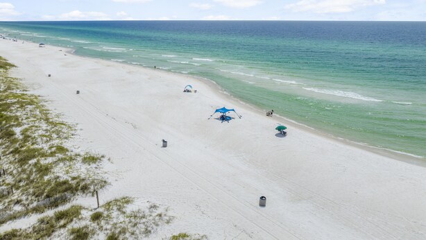 A beach with clear skies, calm waters, and a few umbrellas. - Emerald Coast Paradise Condo, Steps from PCB Beaches! (Panama City Beach)