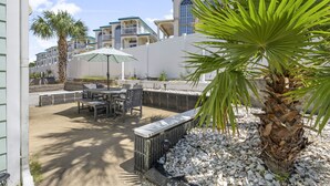 A patio area with outdoor seating, a palm tree, and a view of multi-story buildings in the background. - Emerald Coast Paradise Condo, Steps from PCB Beaches! (Panama City Beach)