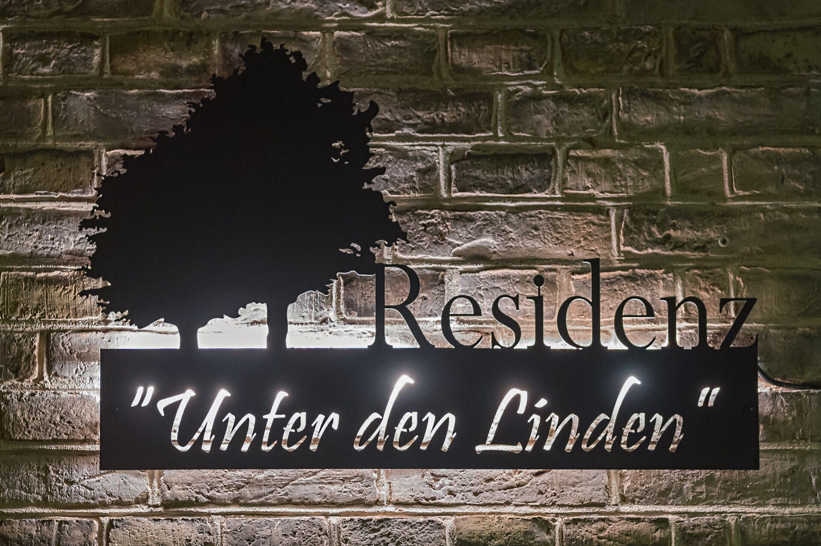 A sign with the word 'Residenz' and the phrase 'Unter den Linden' against a brick wall.