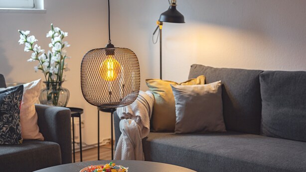 A modern living room with a grey sofa, a round coffee table with a bowl of fruit, a hanging light fixture, and a floor lamp. - Apartment 'Residenz Unter Den Linden Falke' with Wi-Fi (Mühlhausen)