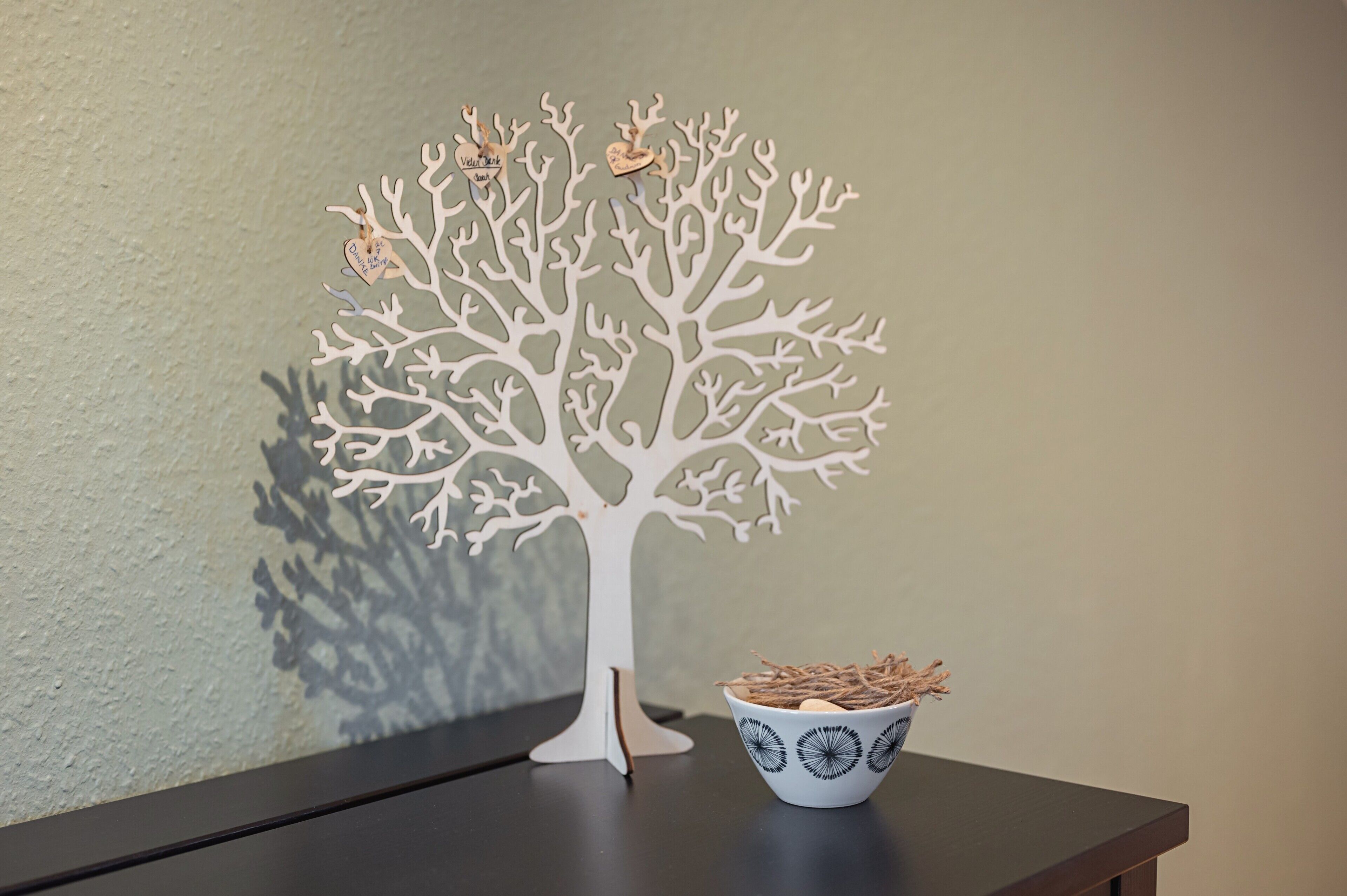 Une décoration blanche en forme d’arbre, ornée d’étiquettes, un bol à motifs bleus et une table sombre.