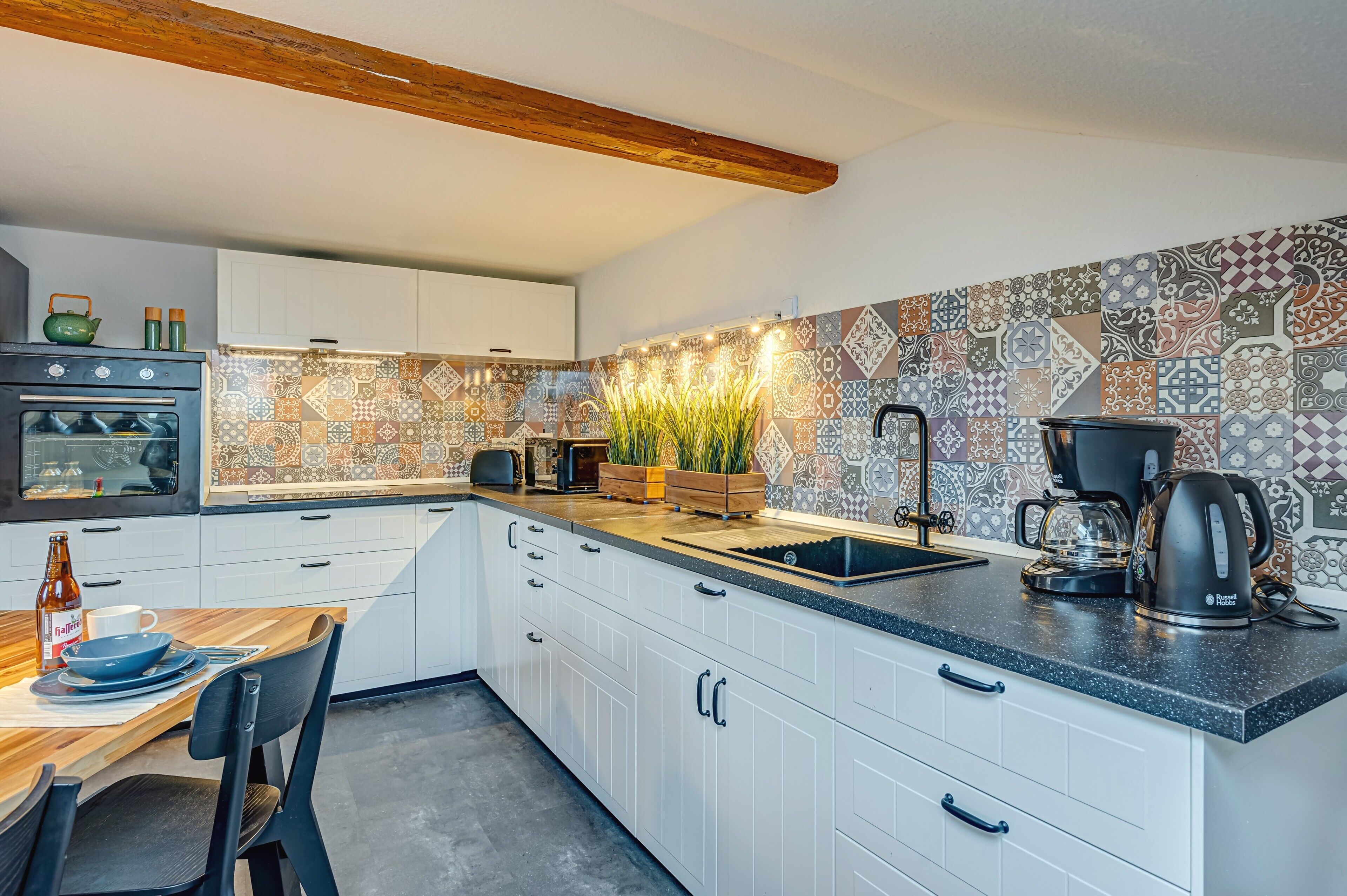 A modern kitchen with white cabinets, a wooden countertop, a built-in oven, and a patterned backsplash.