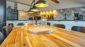 A modern kitchen with a wooden dining table, pendant lights, and a patterned backsplash. - Apartment 'Residenz Unter Den Linden Falke' with Wi-Fi (Mühlhausen)