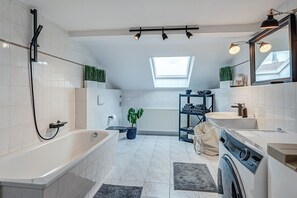 Une salle de bain moderne équipée d’une baignoire, d’une douche, d’un lavabo et d’un lave-linge.