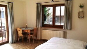 Una camera da letto con un letto, una scrivania con una sedia, una finestra con tende e un termosifone.