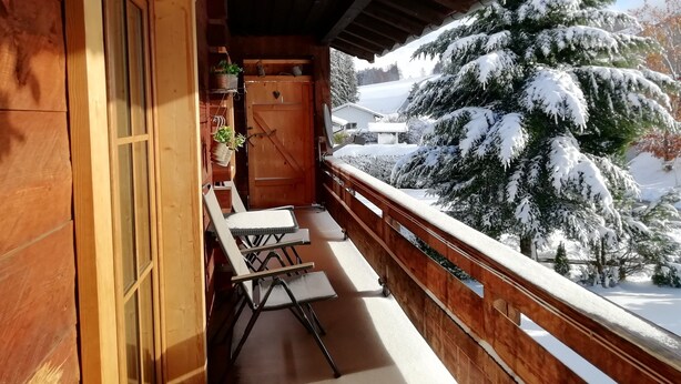 Un balcone in legno con vista su alberi innevati e una casa sullo sfondo.