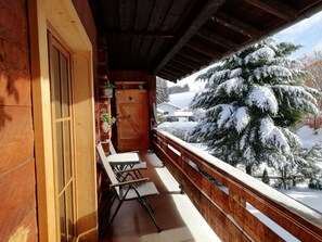 Een houten balkon met zicht op besneeuwde bomen en een huis op de achtergrond.