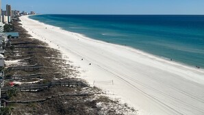 Une plage avec une longue étendue de sable, une mer bleue et limpide, et quelques bâtiments qui bordent le rivage.